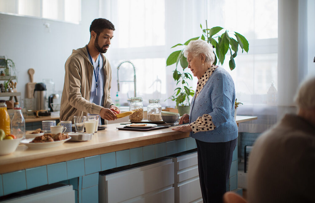 caregiver serving senior woman food in nursing home cafeteria 1200 776