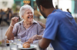 senior woman eating laughing with caretaker 1431924786 1200 776