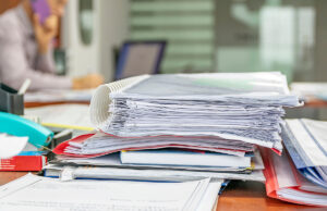 stack of files on desk woman in background 1433094233 1200 776