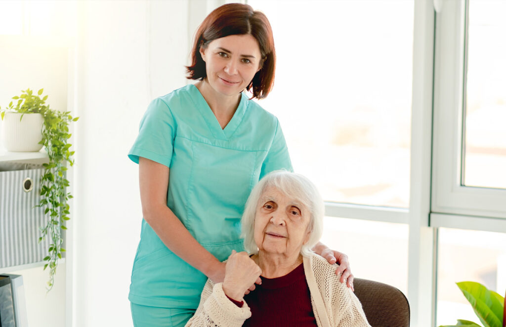 caregiver standing beside elderly woman on chair 1200 776