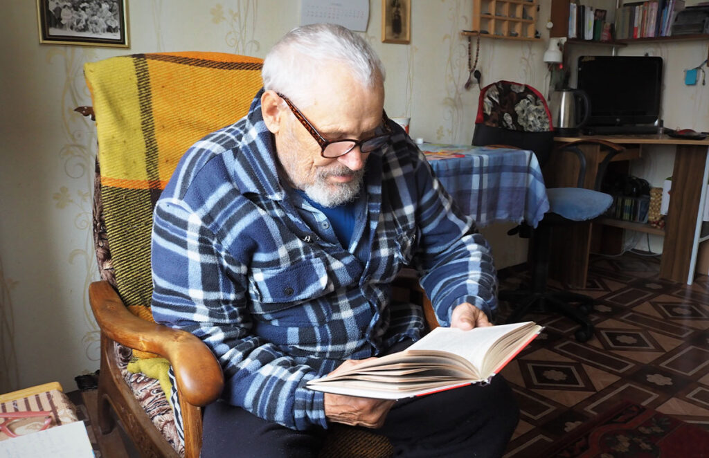 elderly man reads a book sitting in a comfortable chair 1200 776