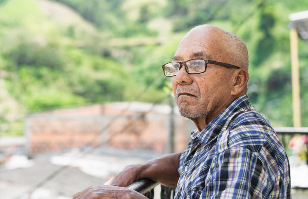 elderly man with brown skin and glasses standing outdoors 1200 776