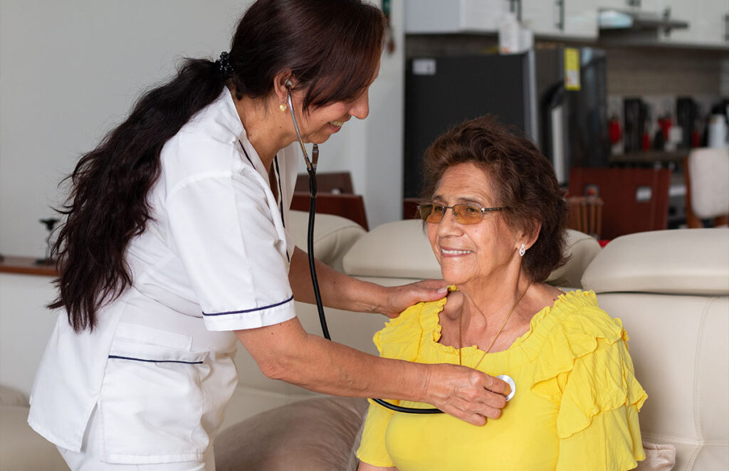 nurse examining an elderly woman with a stethoscope 1200 776