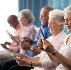 row of smiling senior people sitting on chairs using tablets 1200 776