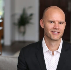 Scott Code smiling wearing a black suit and white polka dotted shirt